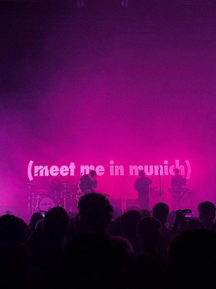 The picture shows a concert photo of the band Royel Otis, taken by Sara Vukman. The photo features the band performing on stage with vibrant magenta lighting, creating a visually striking atmosphere.
