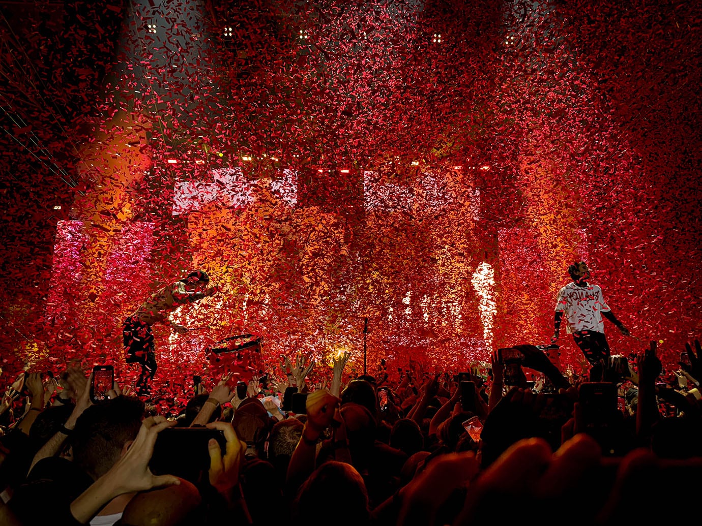 The picture shows a concert photo of the band Twenty One Pilots, taken by Sara Vukman. The photo captures the energy and atmosphere of the live performance, with the band members on stage and the crowd in the background. The lighting and composition highlight the dynamic nature of the concert experience.