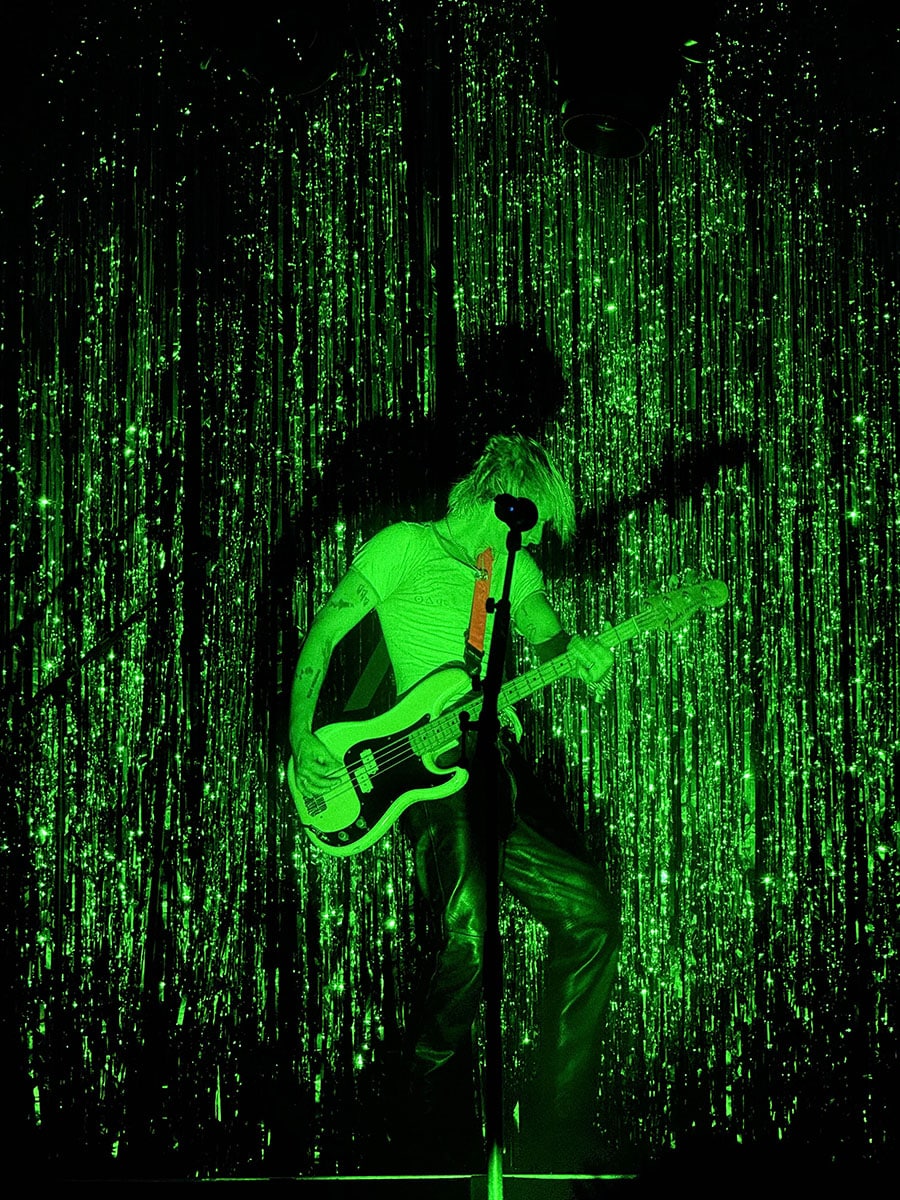 This picture shows a concert photo of the band Wolf Alice, taken by Sara Vukman. The photo features the bassist performing on stage with green lighting.